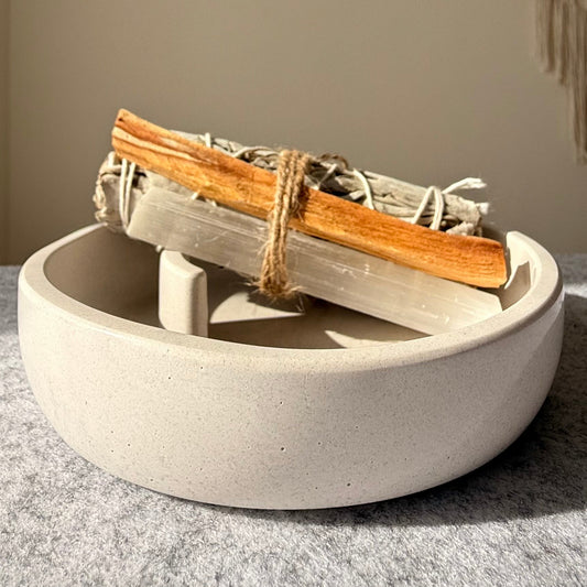 A handcrafted tray made of white stone, with a bundle of white sage and a Palo Santo stick bound by a string, resting on the tray. Selenite stick. by Grace and Gaia